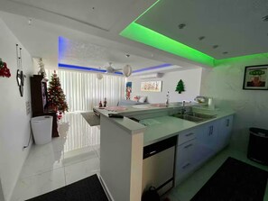 Una cocina moderna con una isla central, armarios blancos e iluminación verde bajo los gabinetes.