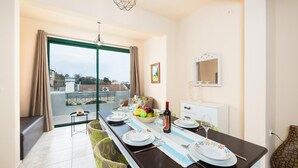 A dining area with a table set for two, a view of the city through large windows, and a balcony with a chair. - Villa Yvonne - Three Bedroom Villa, Sleeps 6 (Kefalas)