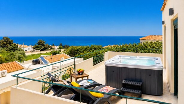 A balcony with a hot tub, lounge chairs, and a table with a bowl of fruit and a glass. - Villa Yvonne - Three Bedroom Villa, Sleeps 6 (Kefalas)
