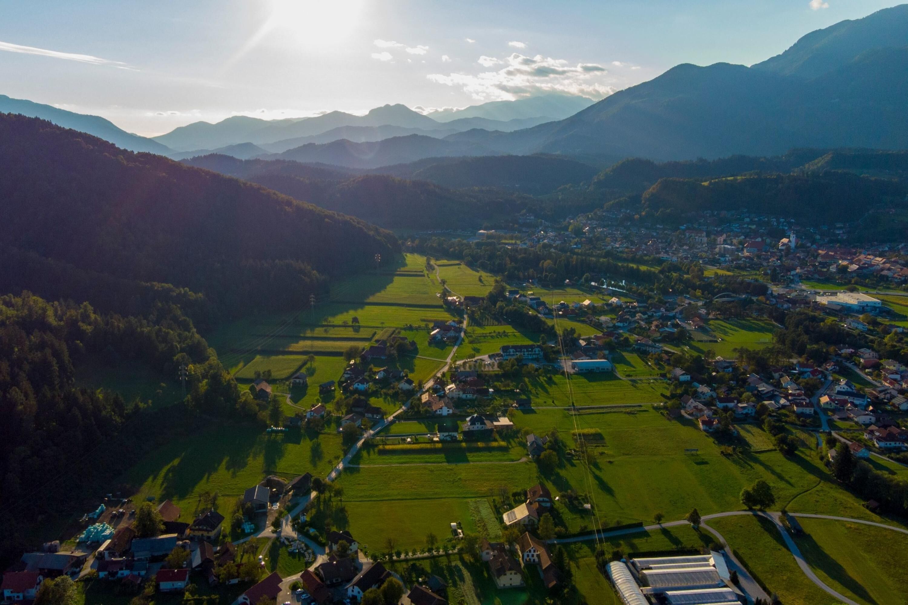 An aerial view of a town with a river, green fields, and mountains in the background.