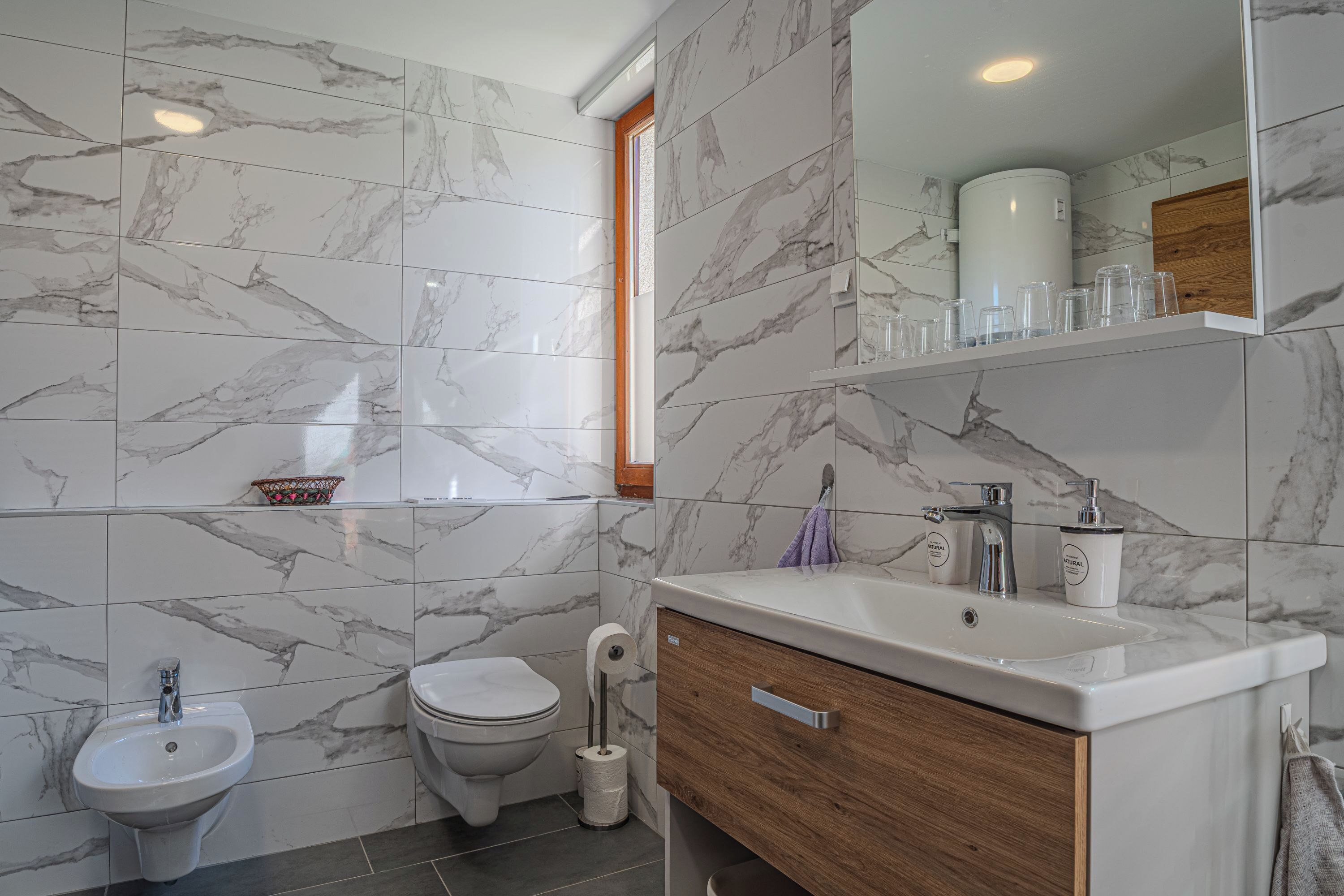 A bathroom with marble tiles, a sink, a toilet, and a mirror.