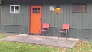A small building with a green exterior, a red door, and two red chairs outside. - Deluxe Cabin B at Elk Creek Escape (Hillsgrove)