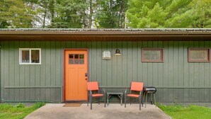A small building with a green exterior, a brown door, and two orange chairs in front. - Deluxe Cabin B at Elk Creek Escape (Hillsgrove)