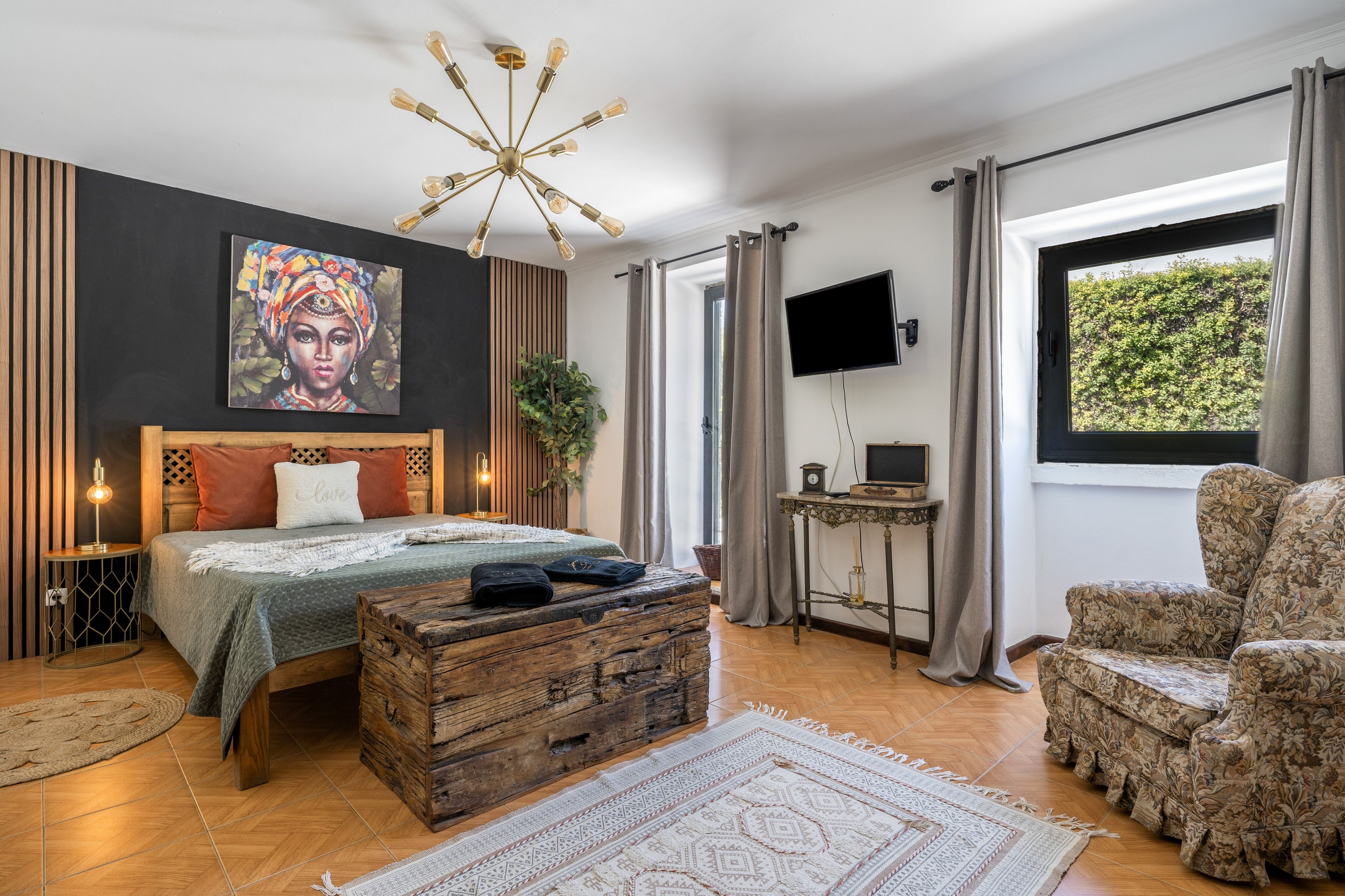 A modern bedroom with a bed, a television, a wooden chest, and a large window.