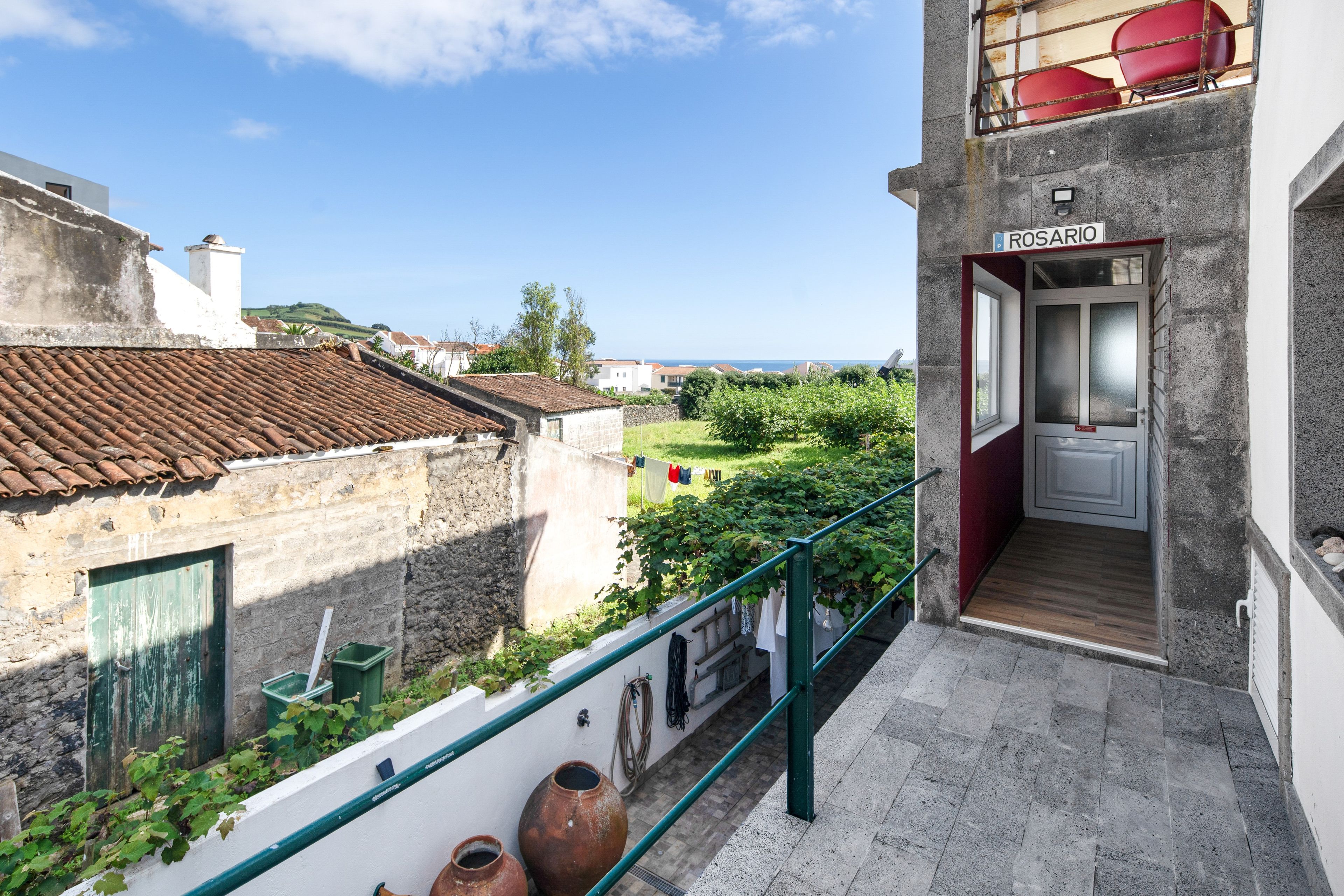 Un balcone con vista sul mare, una porta con la scritta 'ROSARIO' e un piccolo giardino.