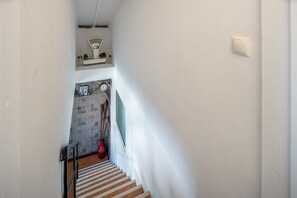 Uma escadaria com corrimão, um relógio fixado na parede e uma prateleira com objetos decorativos.