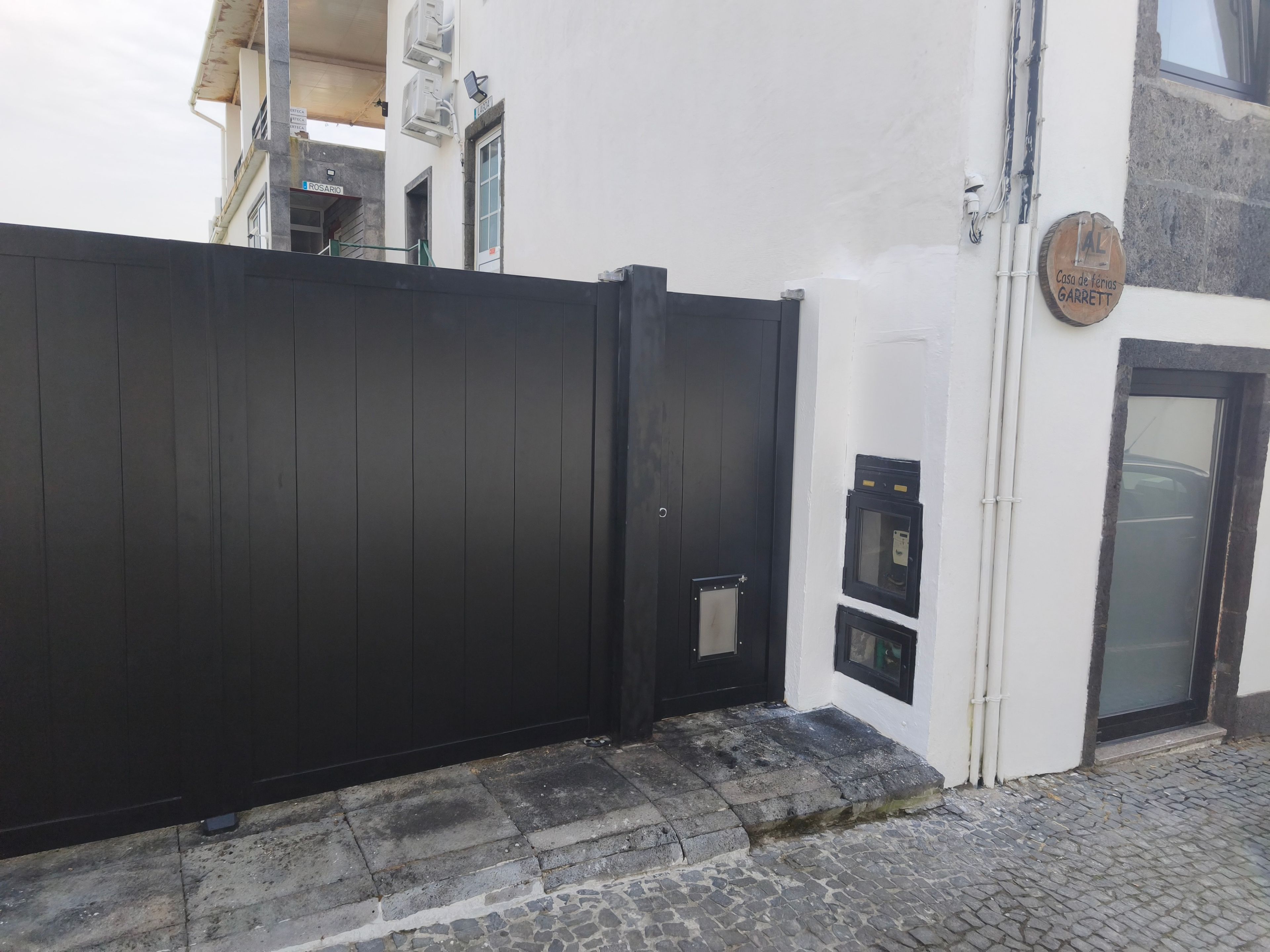 A black metal gate, a white building with a door, and a stone-paved ground.
