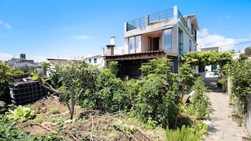 A modern two-story house with a balcony, surrounded by greenery and a garden.