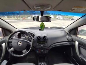 L'intérieur d'une voiture, avec un volant, un tableau de bord, des bouches d'aération et un rétroviseur.