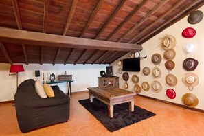 Sala de estar com teto de madeira, sofá preto, mesa de centro de madeira e parede decorada com vários chapéus.