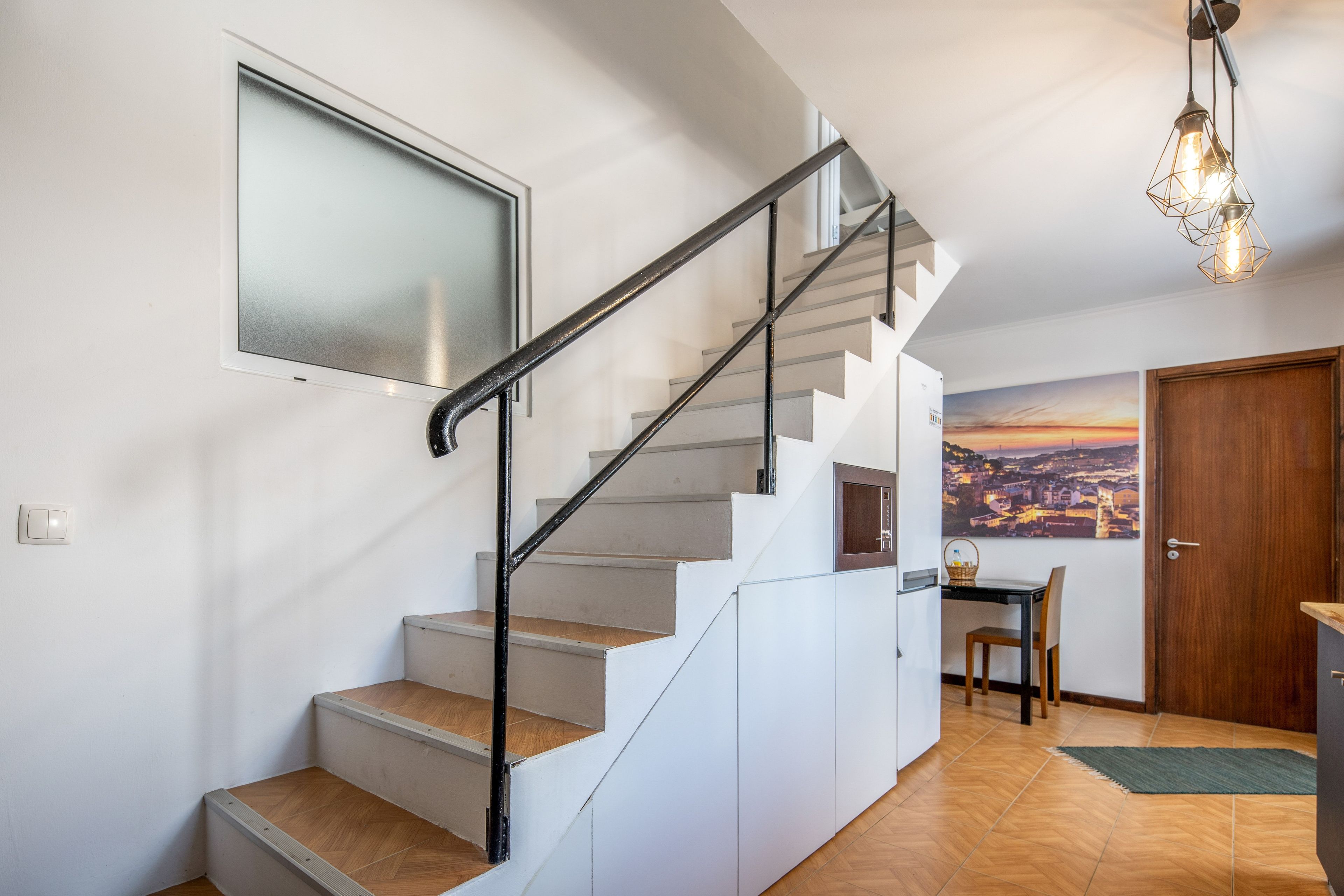 A staircase with a handrail, a dining area with a table and chairs, and a door.