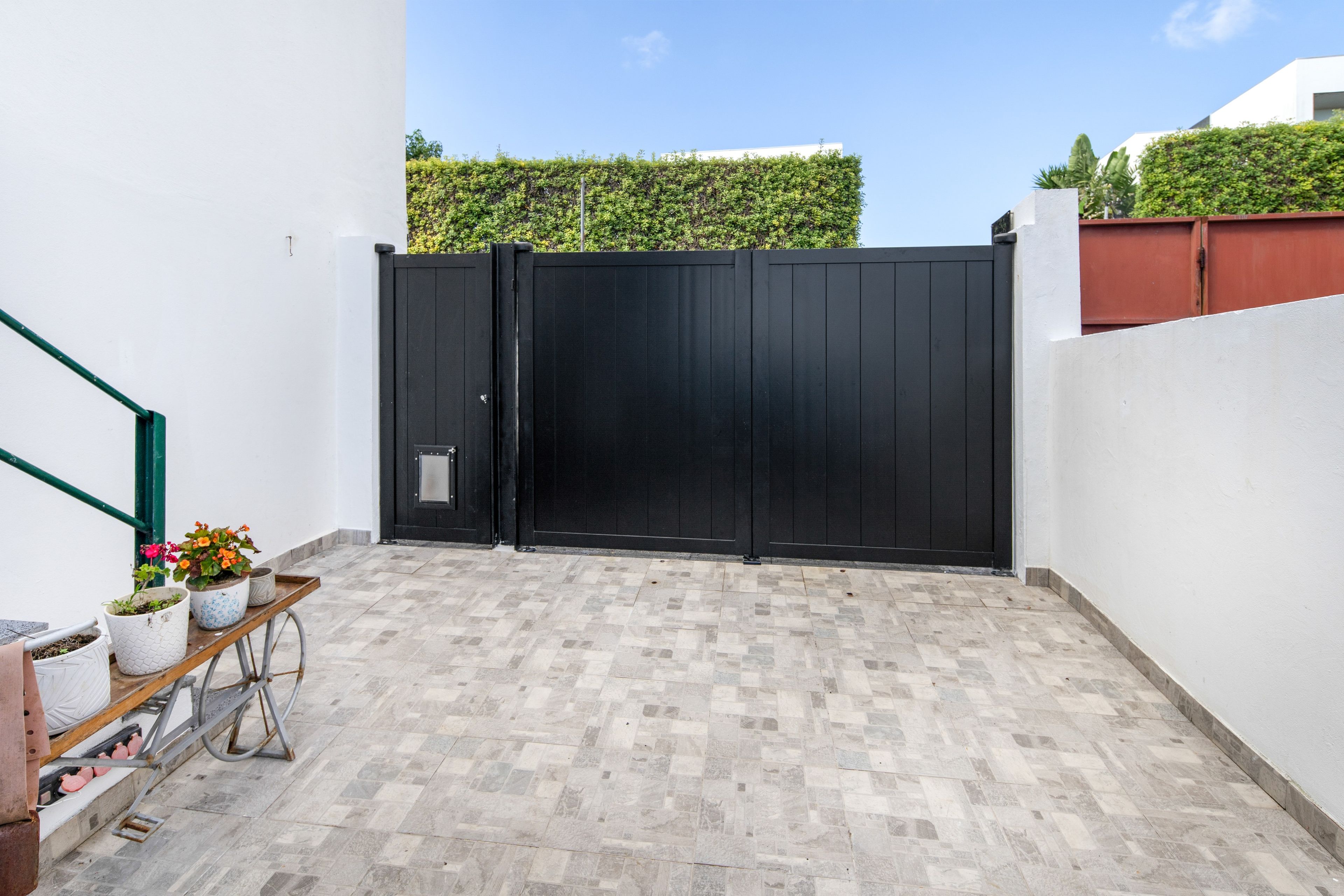 Un patio amurallado con suelo de baldosas y un banco de metal con plantas en macetas.