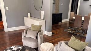 A modern living room with a grey wall, a round mirror, a white console table, and a dining area with brown chairs. - ATL Movie House, Theater Room, Sleeps9, Near Downtown (Atlanta)