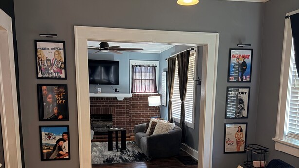 A living room with a dark-colored sofa, a fireplace, and a television mounted on the wall. - ATL Movie House, Theater Room, Sleeps9, Near Downtown (Atlanta)
