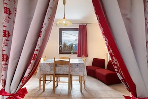 Un coin repas avec une table dressée pour deux personnes, un canapé rouge et une fenêtre donnant sur les montagnes.