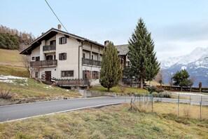 Un bâtiment à deux étages doté de balcons, d’une allée pavée et surplombant un paysage montagneux.