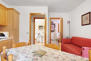 Une pièce comprenant un lit, un canapé rouge, des meubles en bois, un four à micro-ondes et une porte donnant sur une autre pièce.