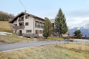 Un bâtiment à deux étages doté de balcons, d’une allée pavée et surplombant un paysage montagneux.