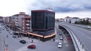 A hotel with a modern glass facade, located at a busy intersection with a pedestrian crossing and a bridge overhead. - Kent Room Hotel (Kapaklı)