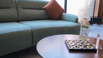 A modern living area with a green sofa, a brown pillow, a wooden table with a QR code, and a small wooden game board.