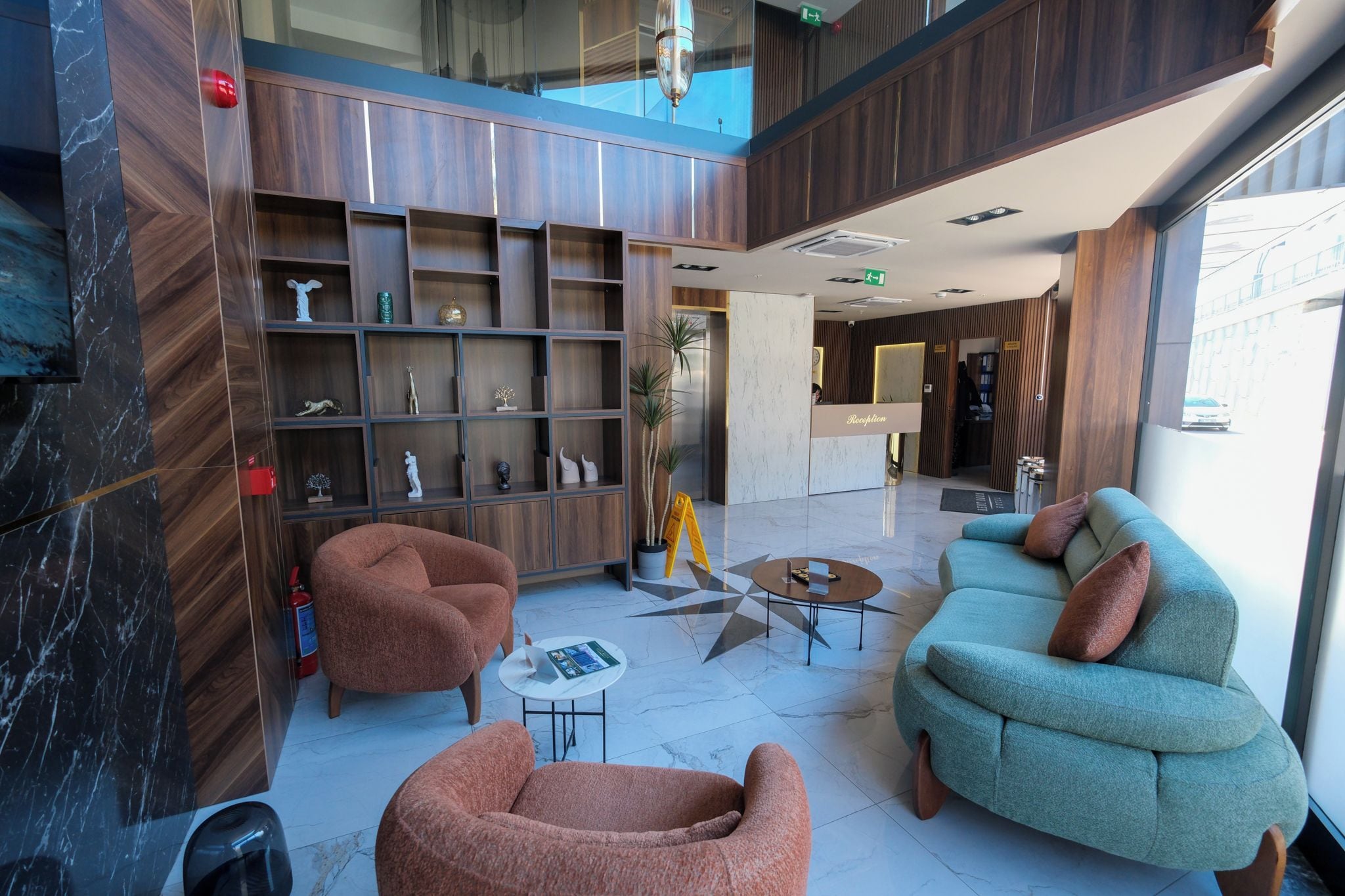 A modern lobby with a reception desk, seating area, and a large wooden shelving unit.