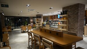 A modern cafe with a long wooden table and chairs, a brick accent wall, and a display case with pastries. - Kent Room Hotel (Kapaklı)