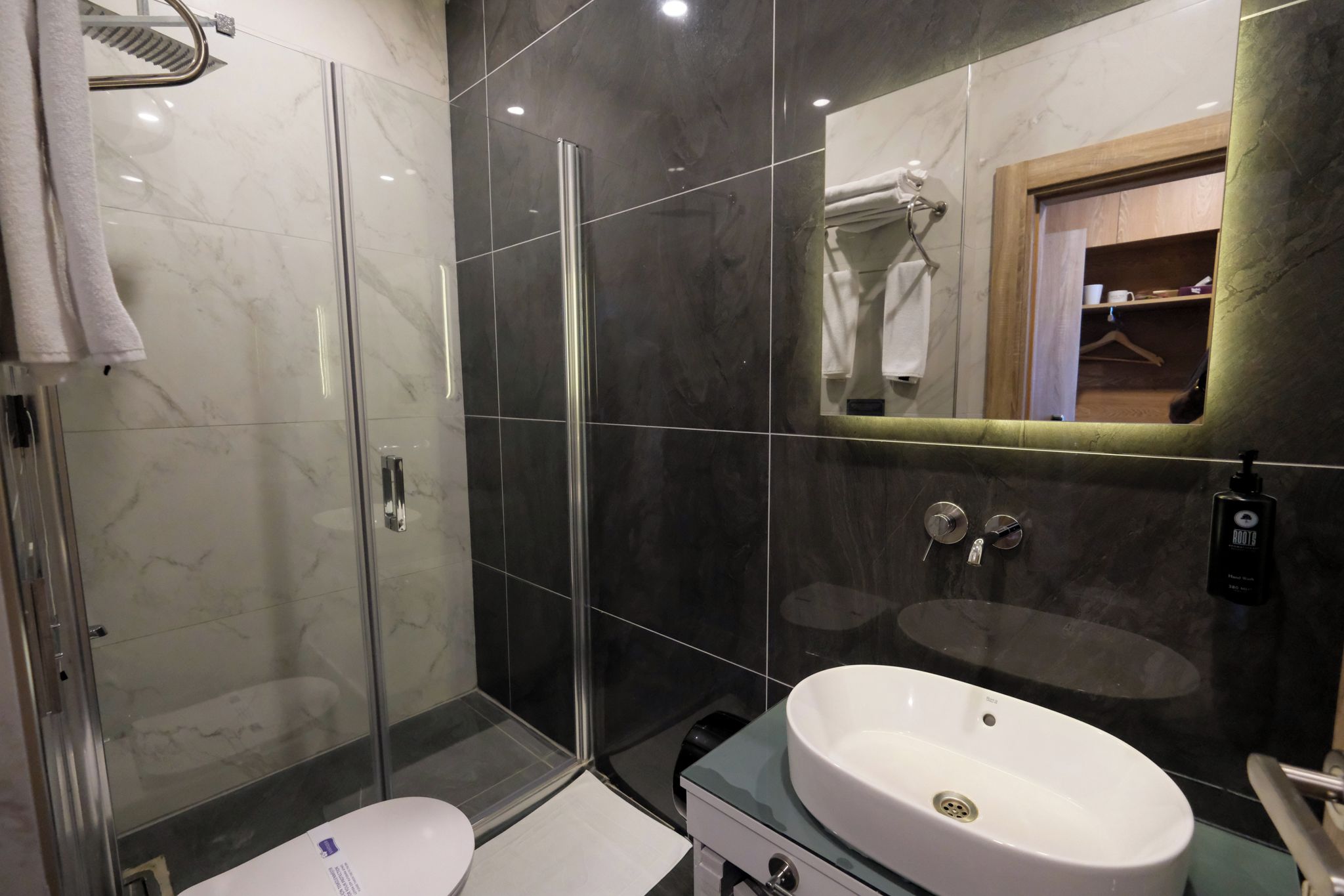 Un baño moderno con cabina de ducha de vidrio, un lavabo blanco y un espejo con marco de madera.