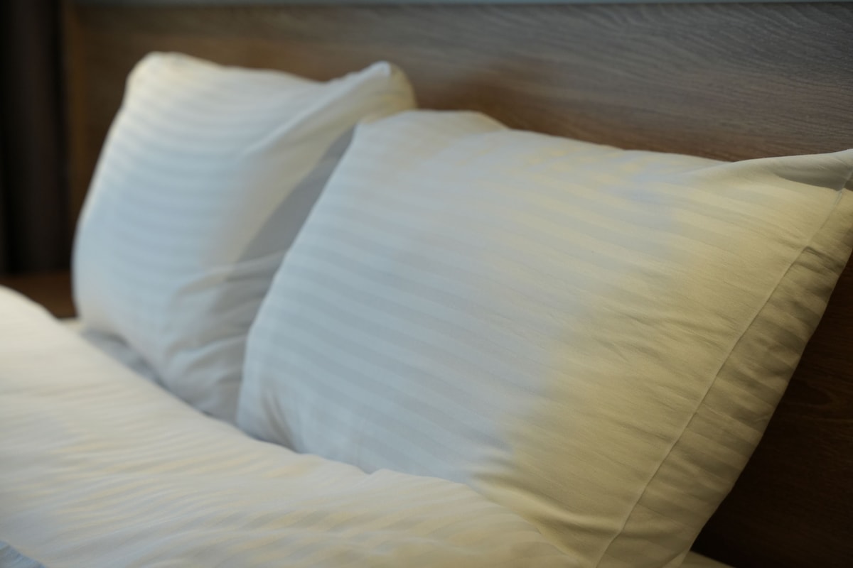 Ein Bett mit weißen Kissen und einem hölzernen Kopfteil.