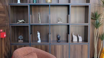 A modern interior with a wooden wall, a brown armchair, a small round table, and a bookshelf with various decorative items.