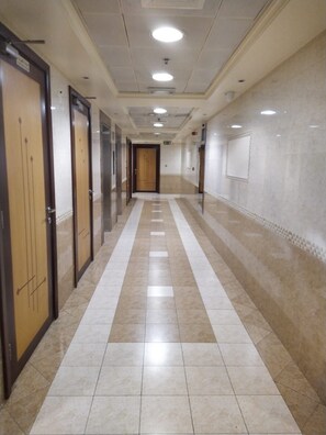 Un couloir d’hôtel avec des portes d’un côté, un sol carrelé et un mur uni de l’autre.