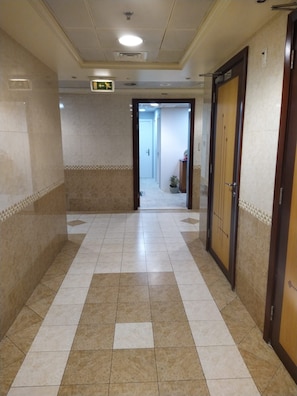 A corridor with tiled flooring, doors on the right, and an exit sign overhead. - Avari Al Barsha Apartment Hotel (Dubai)