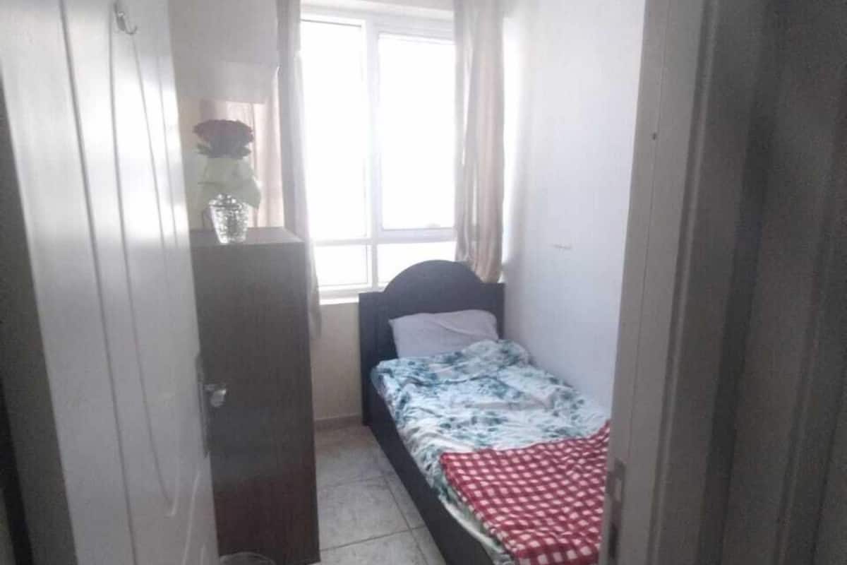 A small, narrow room with a bed, a dresser, and a window.