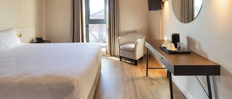 A hotel room with a large bed, a desk with a chair, a flat-screen TV, a mirror, and a window with curtains.