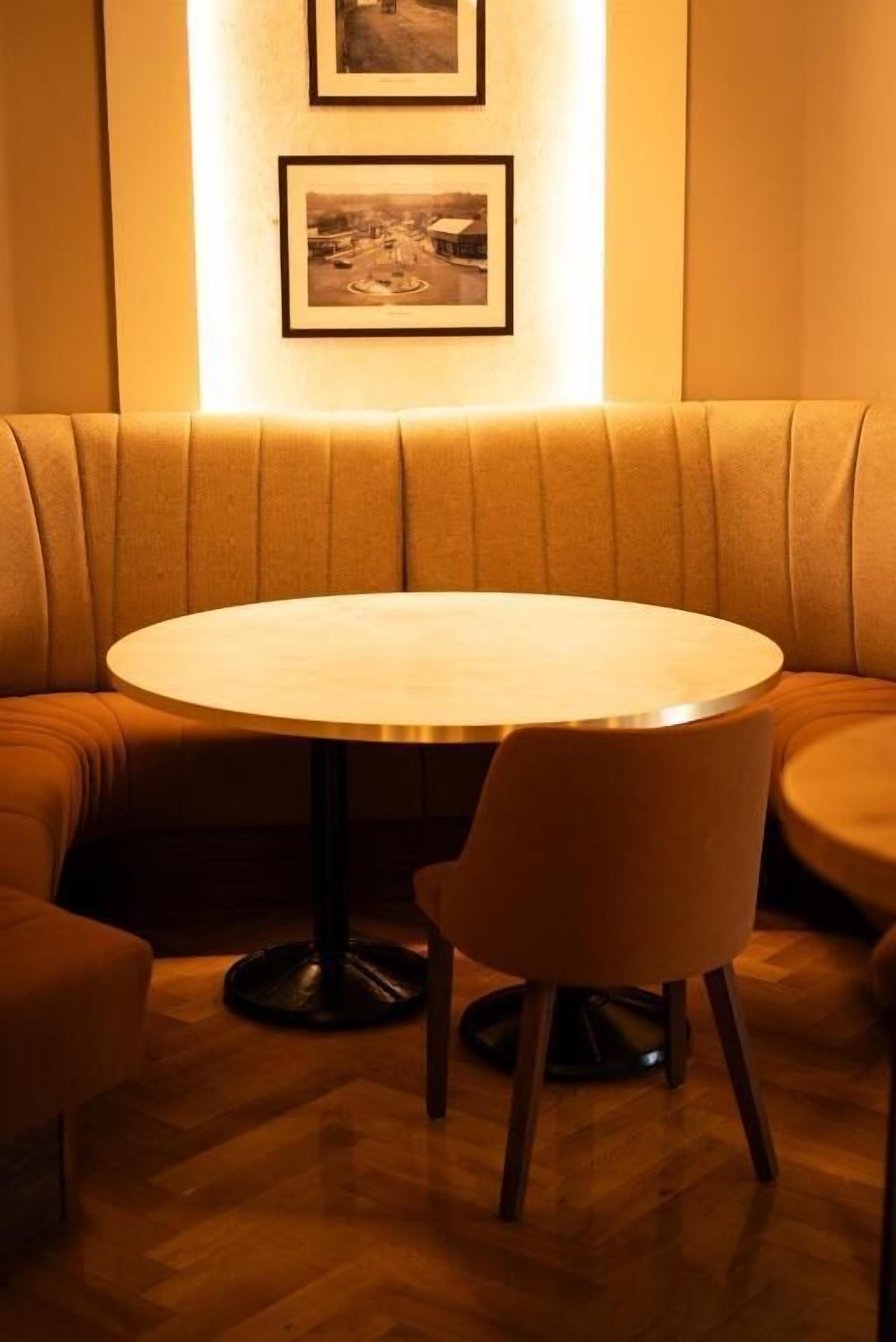 A round table with a single chair in a cozy seating area with cushioned benches.