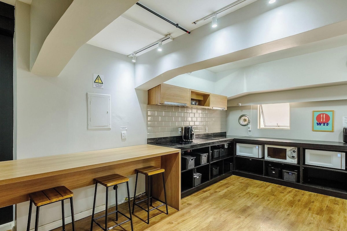 A modern kitchen with a wooden bar and stools, a tiled backsplash, and a black countertop.