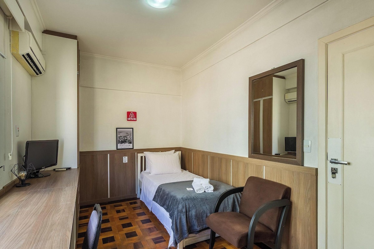 A hotel room with a bed, a chair, a desk with a computer, and a TV.