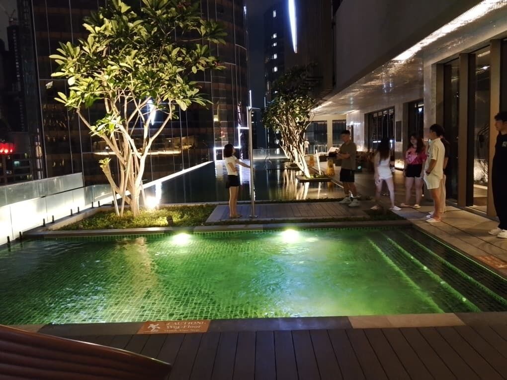 A nighttime pool area with a tiled surface, surrounded by trees and buildings.