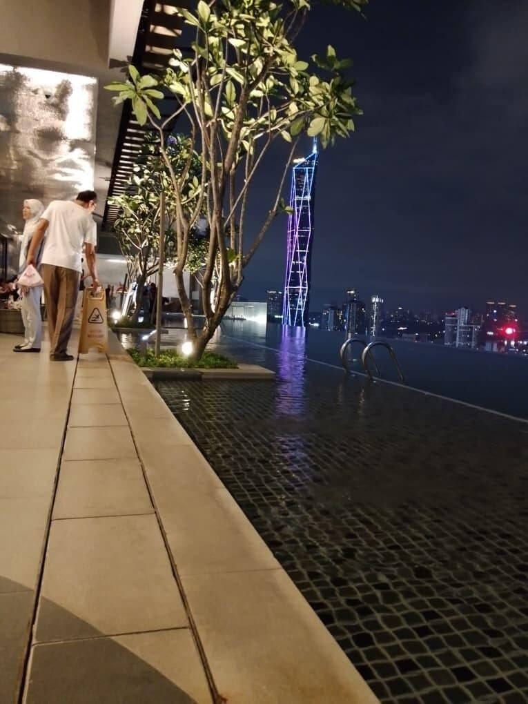 Un espace extérieur agrémenté d’un élément aquatique, d’arbres et offrant une vue sur les lumières de la ville la nuit.