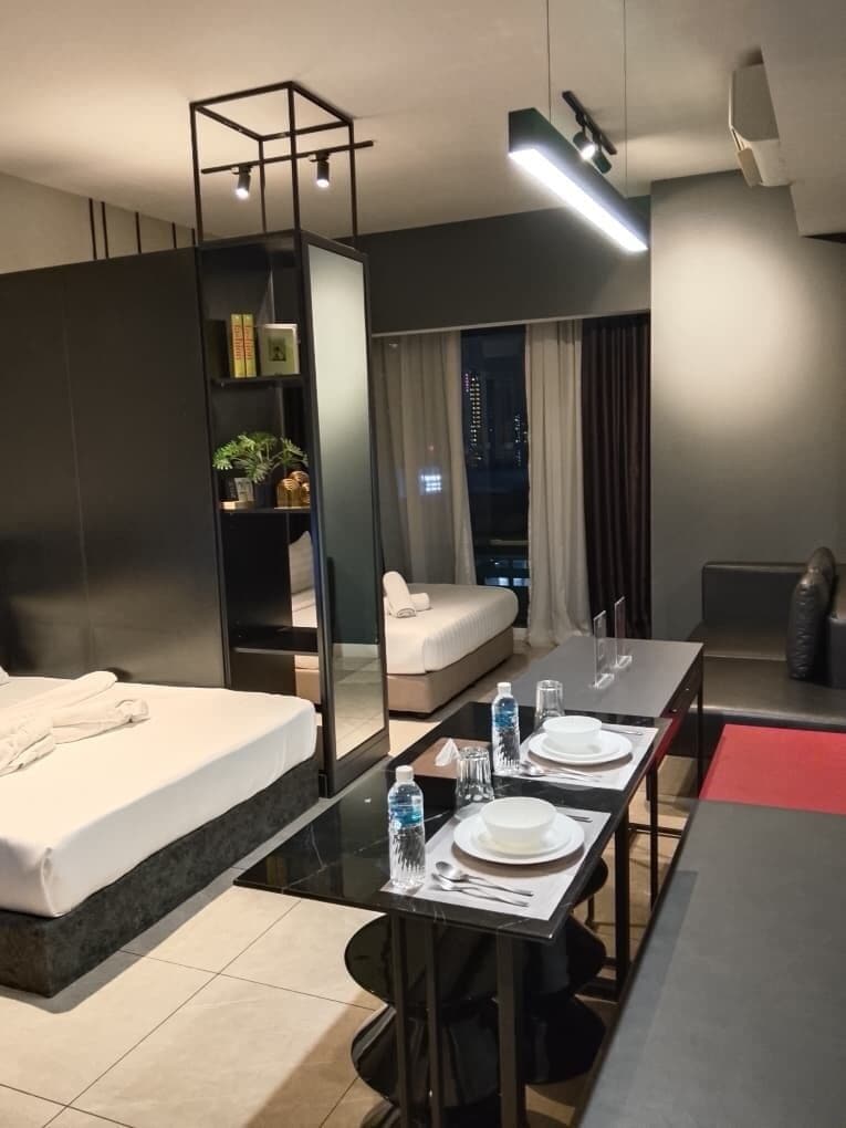 A modern hotel room with a bed, a dining table set for two, a small seating area, and a view of the city at night.