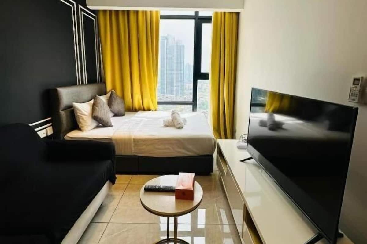 A modern hotel room with a bed, a sofa, a TV, and a window with curtains.