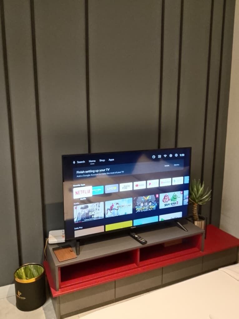 A television on a stand with a red shelf below it, a remote control on the shelf, and a small potted plant to the right.