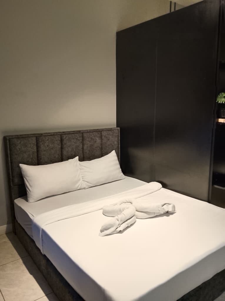 A neatly made bed with white linens and towels, a dark headboard, and a modern wardrobe.