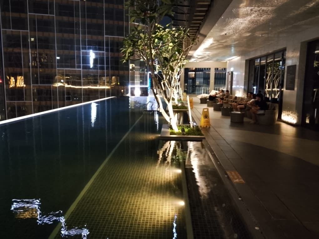 En indendørs swimmingpool med flisekant, omgivet af siddeområder og en moderne bygningselev.