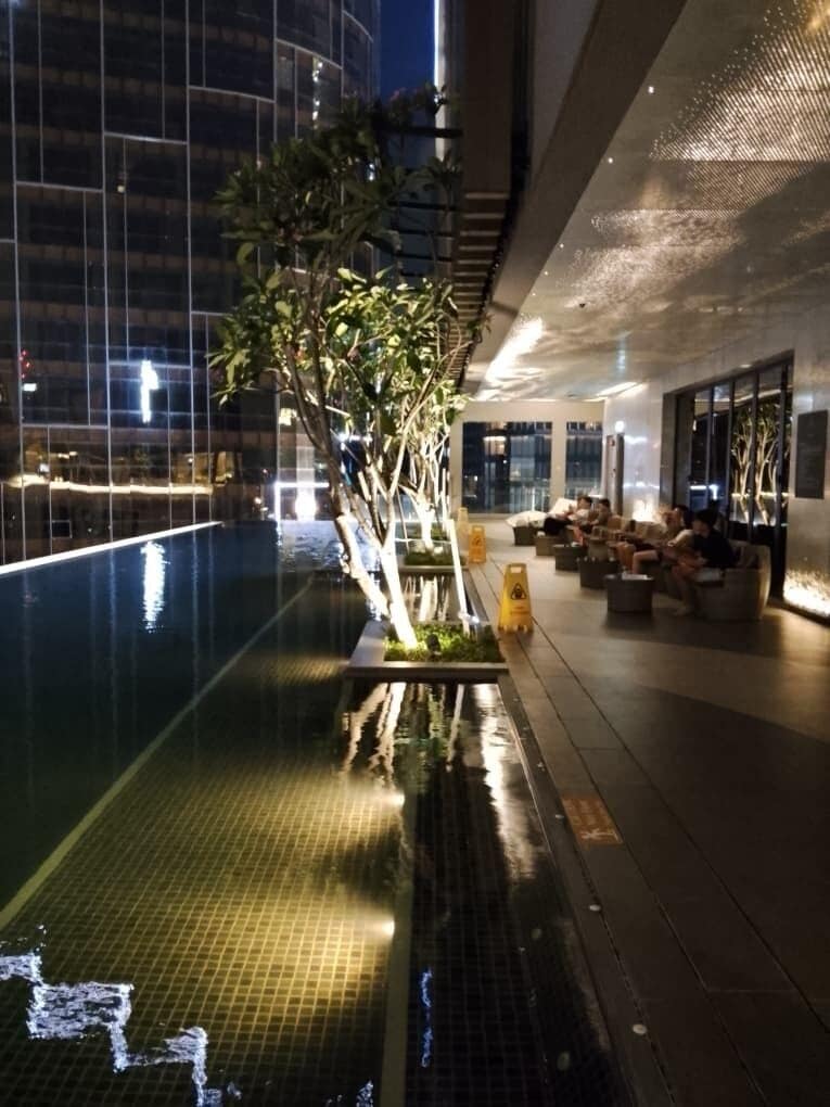 An indoor swimming pool with a glass barrier, seating areas, and a modern building in the background.