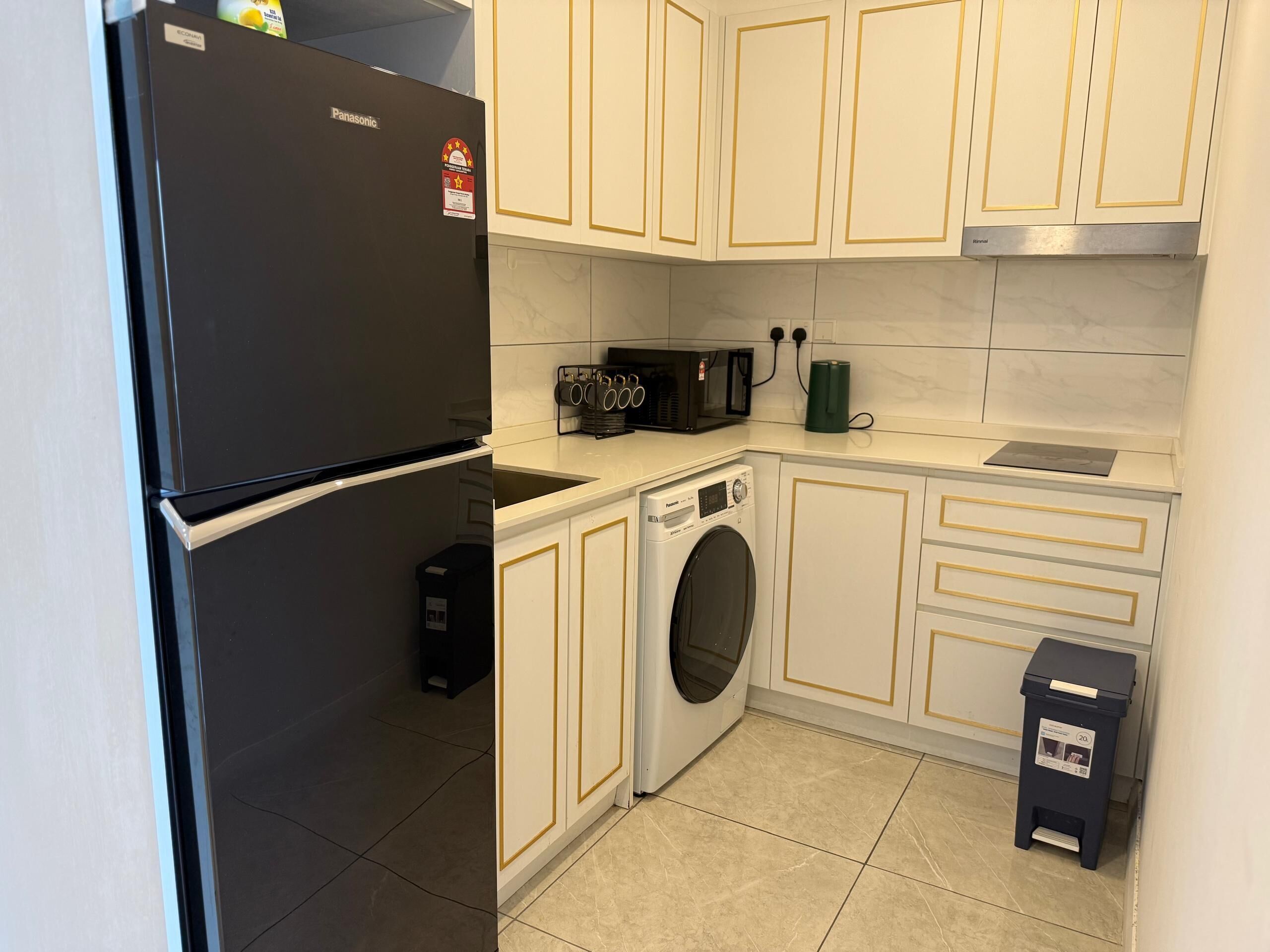 A compact kitchen with a black refrigerator, a washing machine, a microwave, and a trash bin.