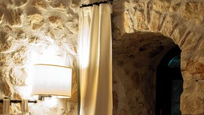A room with a stone wall, a bed with white bedding, a lamp, and a window with a curtain. - L' Armoniosa the magic of the medieval Macchiaroli Castle in Teggiano (Teggiano)