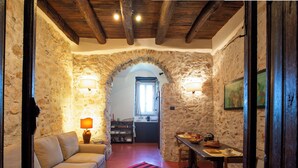 A cozy room with a stone wall, a wooden ceiling, a sofa, a table with chairs, and a red striped rug. - L' Armoniosa the magic of the medieval Macchiaroli Castle in Teggiano (Teggiano)