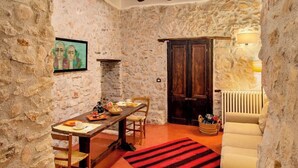 A rustic stone-walled room with a wooden dining table, chairs, a red and black striped rug, and a cozy seating area with cushions. - L' Armoniosa the magic of the medieval Macchiaroli Castle in Teggiano (Teggiano)