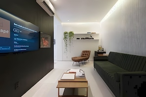 A modern living room with a flat-screen TV mounted on the wall, a sofa, a chair, and a coffee table.