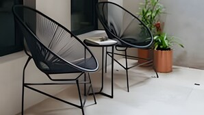 Ein moderner Außenbereich mit zwei schwarzen Stühlen, einem kleinen Tisch, einem Blumentopf und einem großen Fenster.